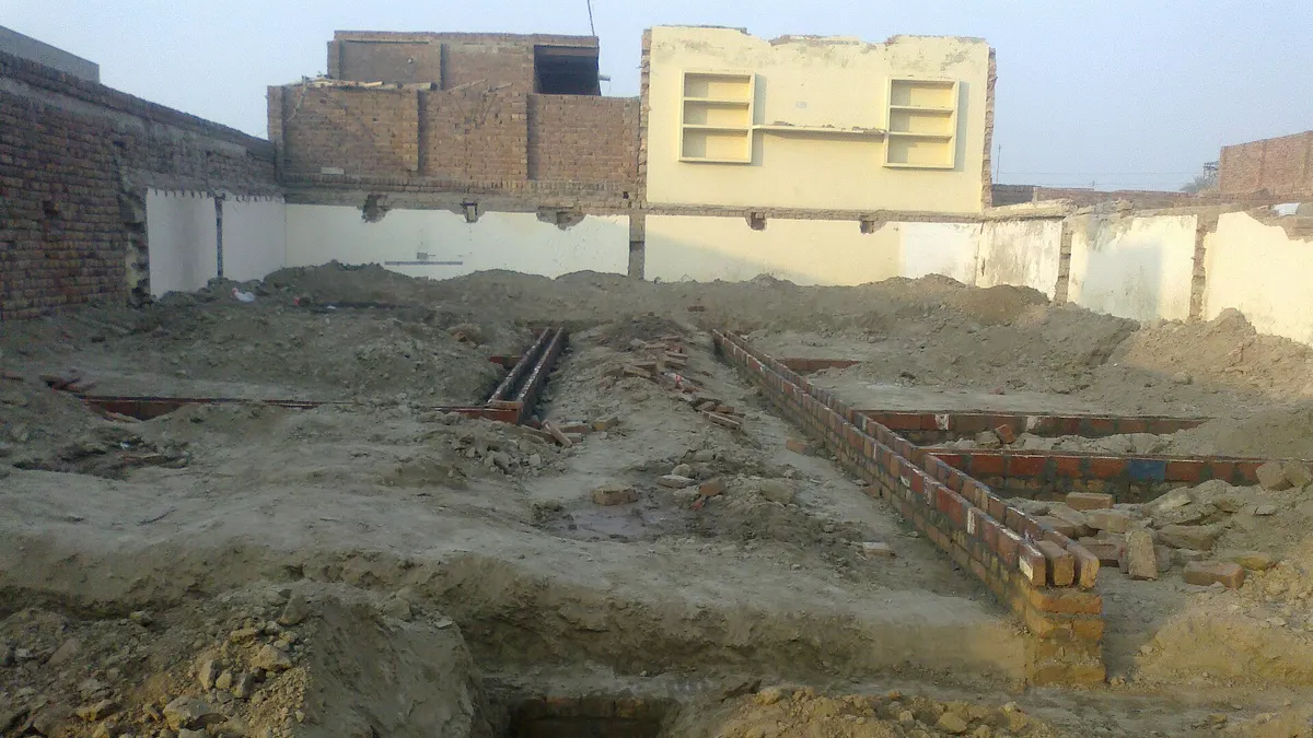 Foundation trenches and brick footings on a narrow house plot between neighbouring walls in Punjab
