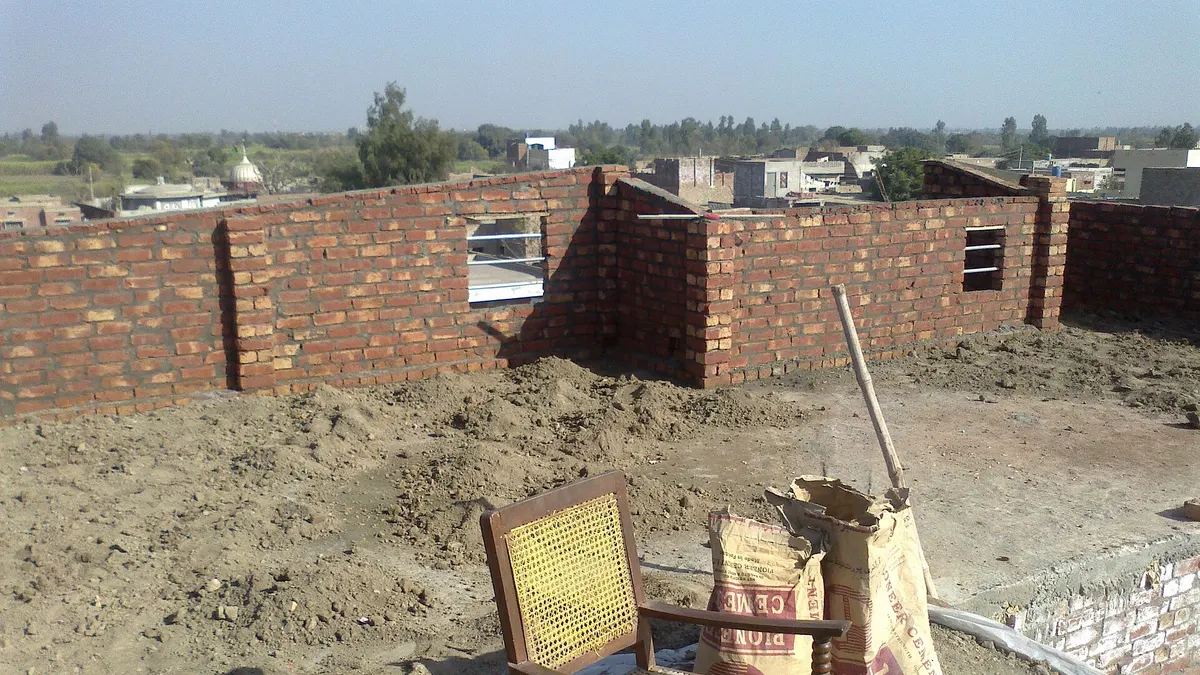 Brick walls of a house going up, with cement bags on the roof slab, in a village near Faisalabad