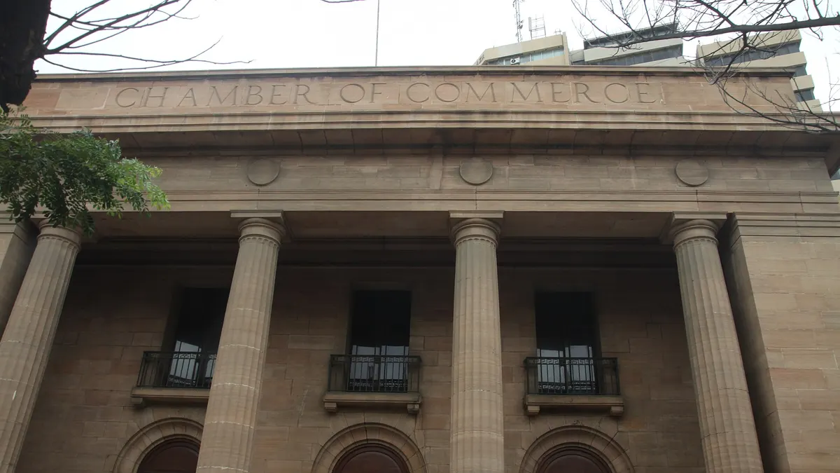 The stone colonnade of a historic chamber of commerce building in Karachi, with 'Chamber of Commerce' carved above the columns