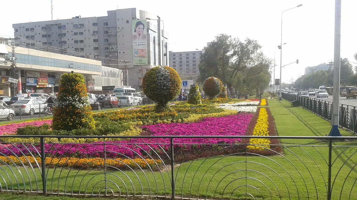 Flower beds and topiary on the median of Main Boulevard, Gulberg, Lahore, near Hafeez Centre, with office blocks and parked cars behind