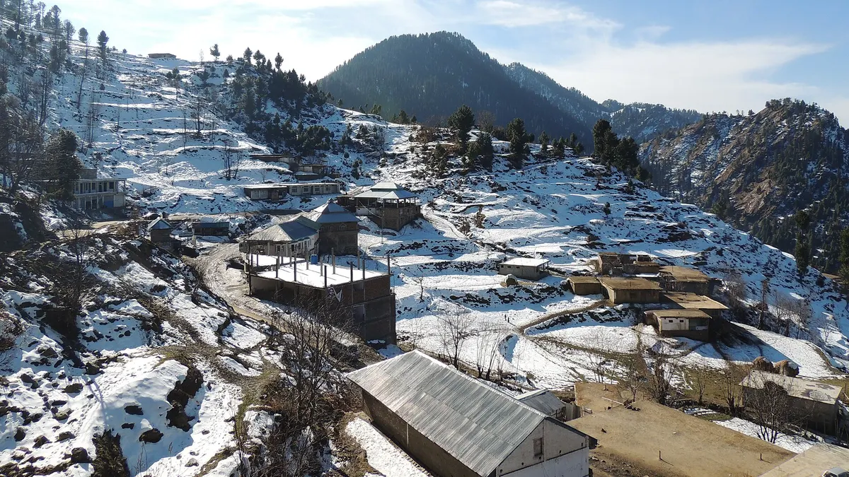 Snow on the slopes and houses of Malam Jabba in Swat, with pine forest on the hills behind