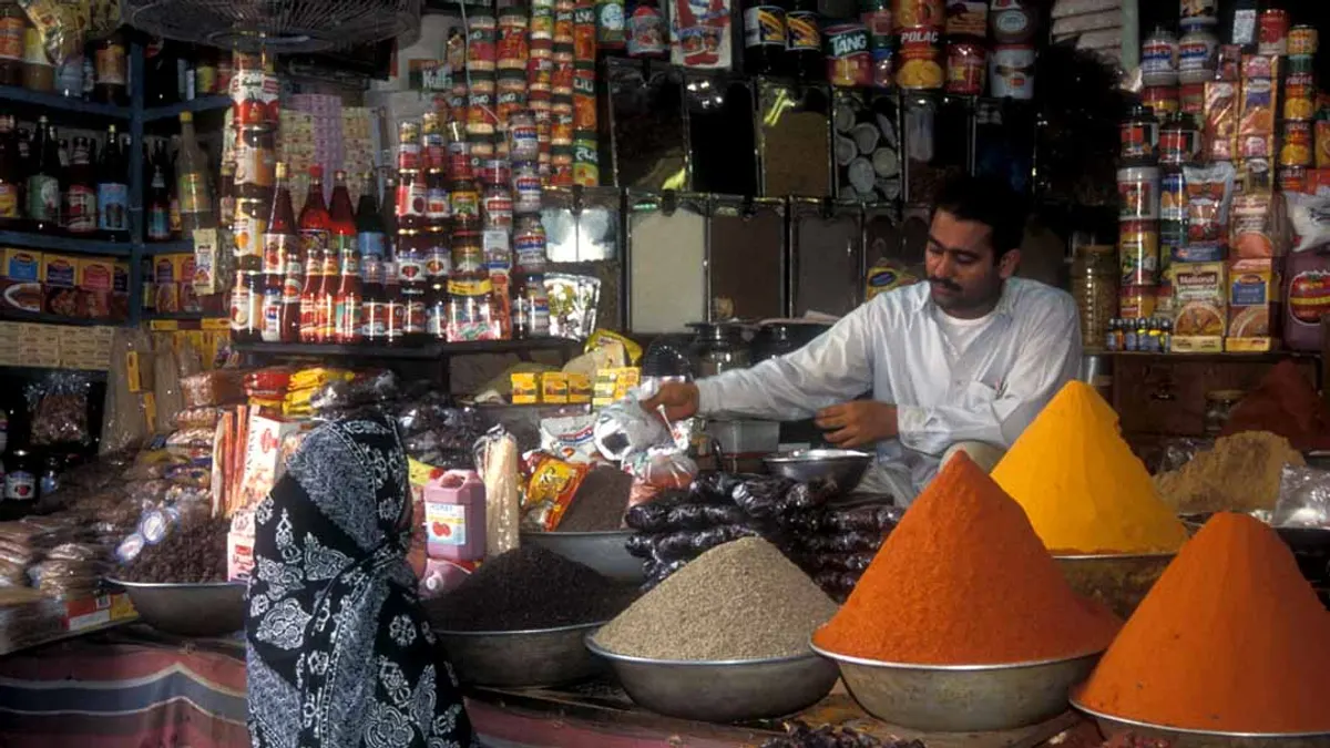 A spice shop in Pakistan with cones of ground spices on the counter and shelves of packaged goods behind the shopkeeper