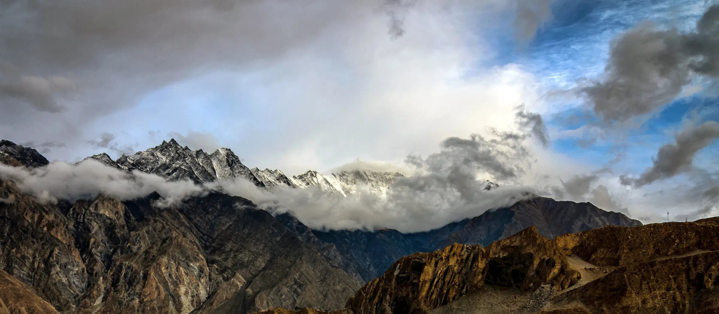 Snow-capped Passu peaks above cloud and brown ridges in Hunza Valley